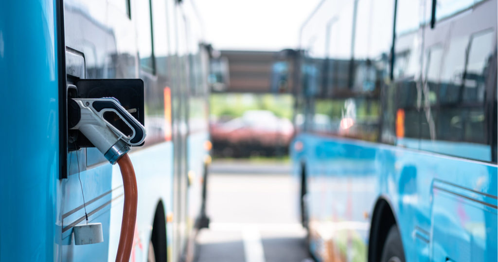 Two blue buses with EV charger plugged in on the left