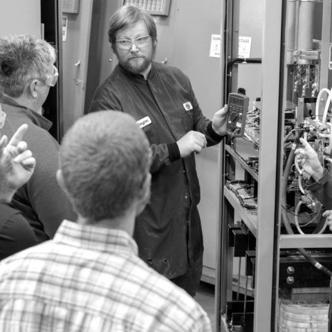 five dynapower employees in safety glasses talk during a training