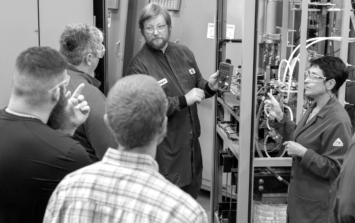 five dynapower employees in safety glasses talk during a training