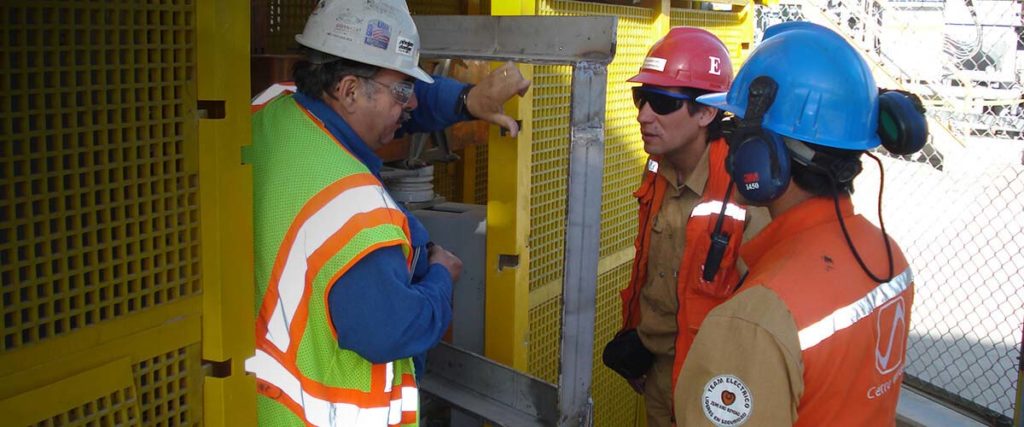 three people in hardhats performing service on machinery