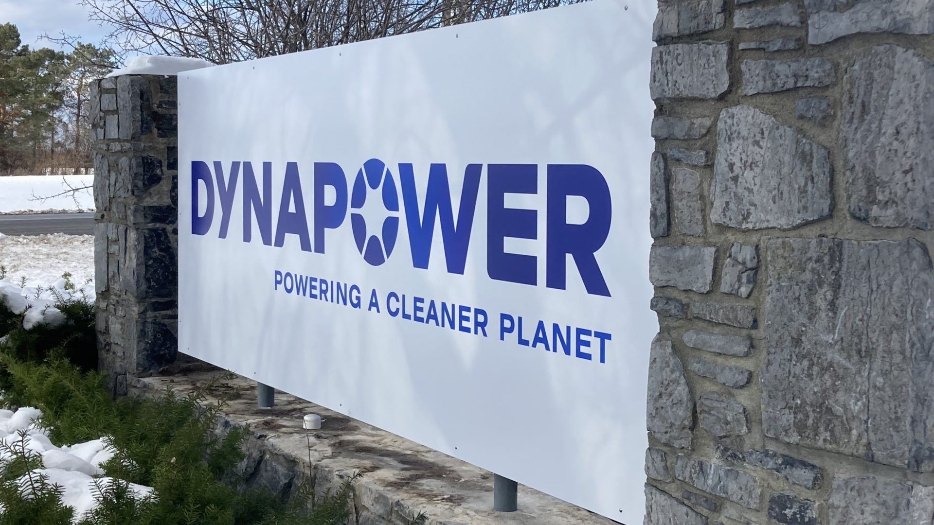 stone wall with white sign that reads "Dynapower, Powering A Cleaner Planet" in blue